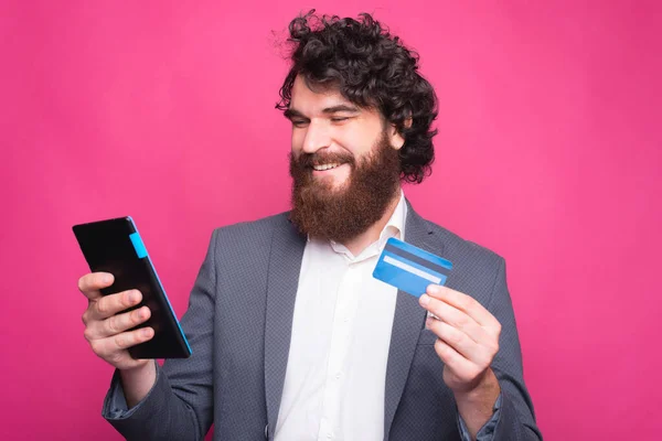 Hombre alegre con barba en traje usando tableta y tarjeta de crédito — Foto de Stock