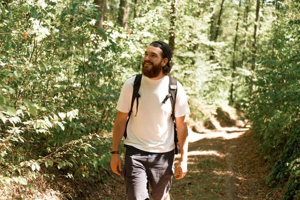 Genç sakallı bir adamın yaz mevsiminde ormanda yürüyüş yaparken çekilmiş fotoğrafı.,