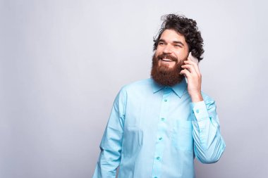 Mavi gömlekli, beyaz duvarın üstünde telefonla konuşan mutlu bir adamın portresi.