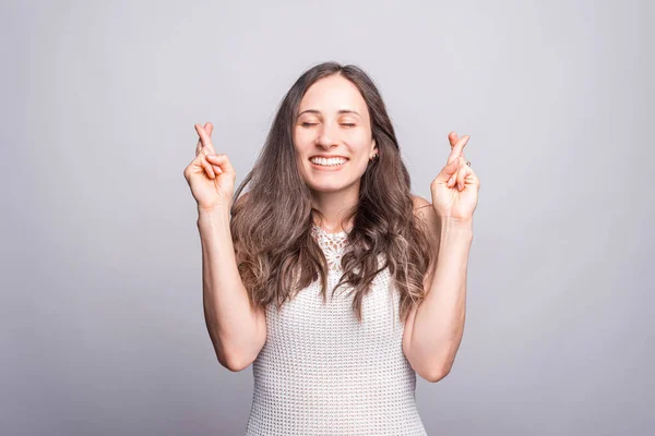 Foto de una joven hermosa mujer de pie sobre la pared blanca con los dedos cruzados y soñando — Foto de Stock