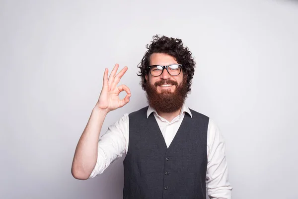 Egy jóképű, vidám, szakállas öltönyös férfi portréja, aki OK gesztust mutat — Stock Fotó