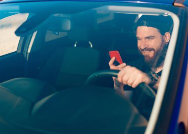 Sakallı, araba kullanan ve telefon kullanan genç bir adamın fotoğrafı.