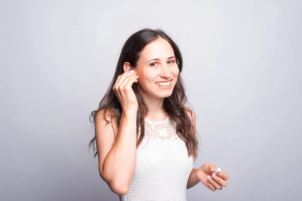 Mujer feliz y sonriente usando auriculares y mirando con confianza a la cámara sobre la pared blanca — Foto de Stock