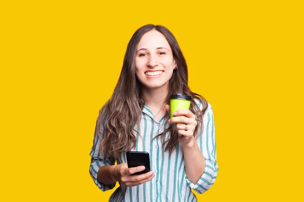 Vrolijk mooi jong vrouw in casual drinken van haar ochtend thee of koffie en het controleren van nieuws op telefoon — Stockfoto