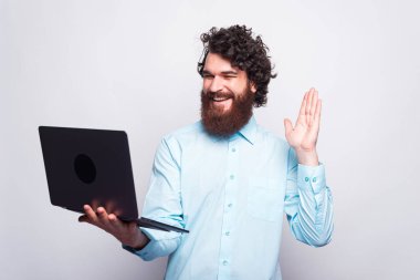 Sakallı neşeli genç adam internette biriyle konuşuyor, evde çalışıyor.