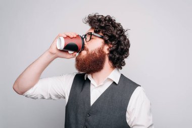 Gri bir duvarın yanında kağıt bardaktan içen genç bir adam.