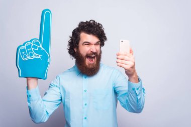 Yelpaze eldivenli ve elinde telefon tutan heyecanlı bir genç adam gri duvarın yanında duruyor.