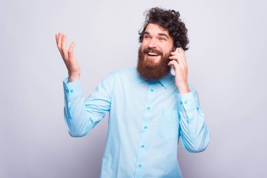 Gri duvarın yanında telefonuyla konuşan genç bir adamın fotoğrafı.