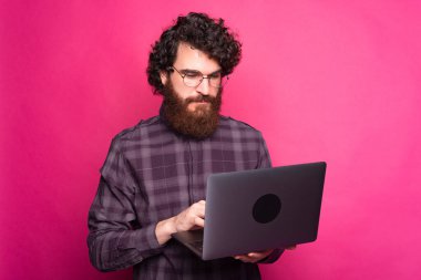 Ciddi bir genç adam elinde bir bilgisayar tutuyor ve ona bakıyor.