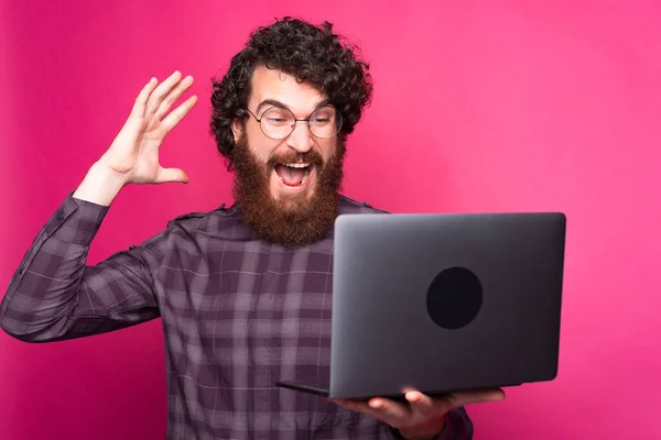 Joven alegre sosteniendo una computadora mirándola emocionada — Foto de Stock