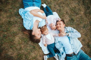 Bebekleriyle birlikte parkta çimlerin üzerinde uzanan neşeli genç aile fotoğrafı, aile zamanı.