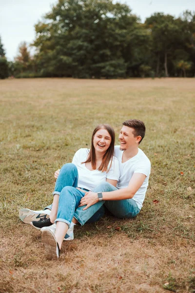 Foto de jovem casal alegre que põe na grama no parque e sorrindo — Fotografia de Stock
