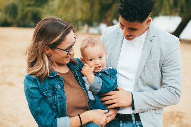 Neşeli genç bir aile bebeklerini kucağına alıp ona gülümsüyor.