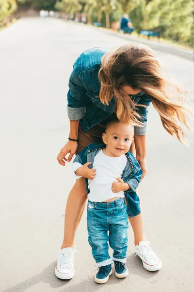 A young woman holding her baby on his feet and he is looking and smiling at the camera — Stock Photo, Image