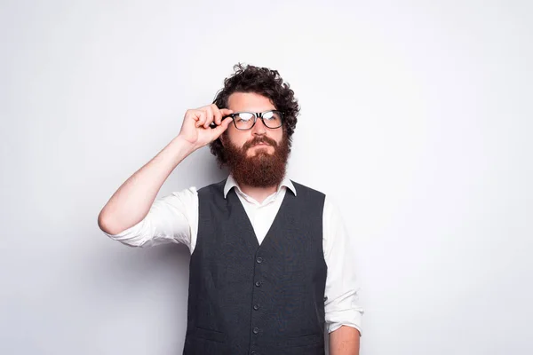 Retrato de hombre barbudo en traje tocando anteojos y mirando en serio lejos — Foto de Stock