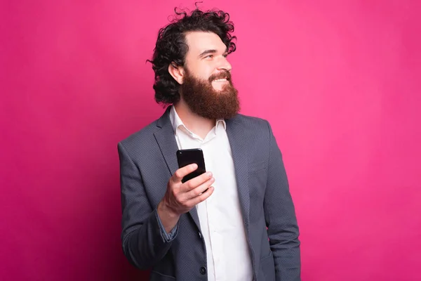 Portrait de beau jeune homme avec barbe est costume tenant le téléphone intelligent et regardant loin de l'espace de copie — Photo