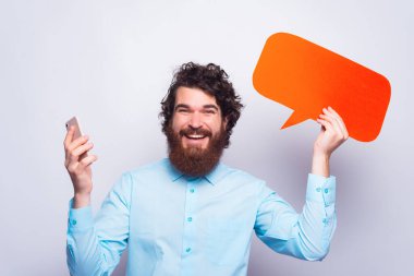 Akıllı telefon ve boş konuşma balonu tutan neşeli genç adamın portresi.