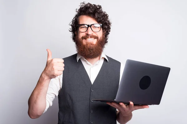 Retrato de un joven barbudo de traje mostrando el pulgar hacia arriba y sosteniendo la computadora portátil — Foto de Stock