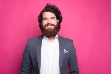 Klasik takım elbiseli neşeli, sakallı bir adam gülümsüyor ve kameraya bakıyor.