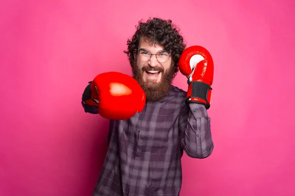 Giovane uomo barbuto e allegro con guanti da boxe e occhiali sta guardando la fotocamera — Foto Stock