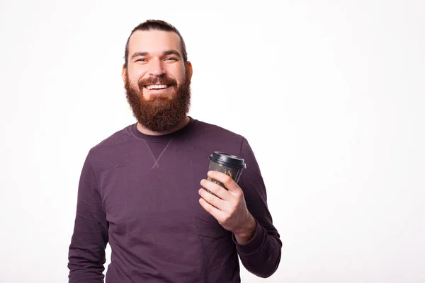 Jeune homme barbu sourit à la caméra et tenant une tasse de boisson chaude esprit — Photo