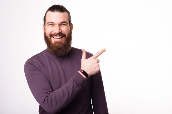 Un jeune homme joyeux sourit à la caméra et pointe du doigt un espace libre neae un mur blanc — Photo