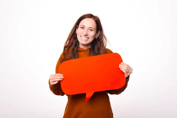 Vrolijke jonge vrouw lacht naar de camera en houdt een spraakbel in de buurt van een witte muur — Stockfoto