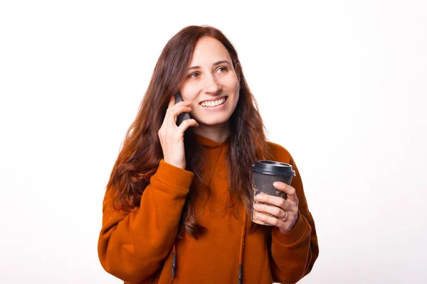 Joven buena mujer está hablando con su teléfono y sosteniendo una taza de agua caliente está mirando y sonriendo — Foto de Stock