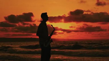 Gün batımında sakin sahilde tutkuyla çalan yetenekli bir saksafoncunun büyüleyici silueti.