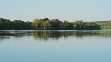 Güzel ve huzurlu bir nehir manzarası, berrak mavi gökyüzünün altında yemyeşil ve huzurlu yansımalar sergiliyor.