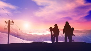 Dağlarda parlak bir gün batımının arka planında bir çift snowboardcu.