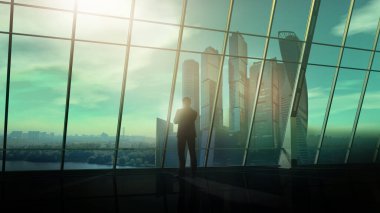 Büyük ofis penceresinin önünde, bir adam duruyor ve uzaklığa bakıyor..