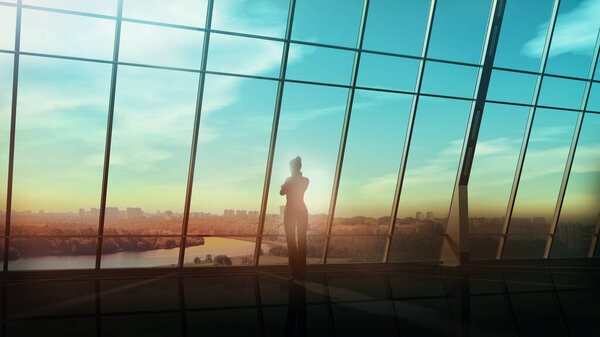 A silhouette of a business woman is looking out of the window of her large office with a view of the city skyline.