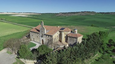 Torquemada 'nın açık yeşil manzarasında kırmızı kiremit çatılı büyük taş inziva yeri.