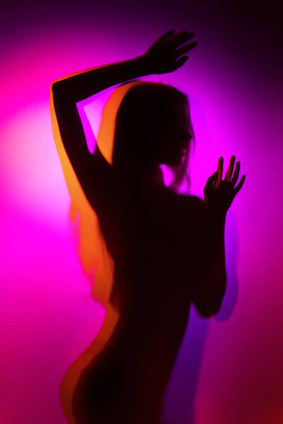 Silhouette of a girl in violet and orange colour light wearing lingerie shot through matte glass