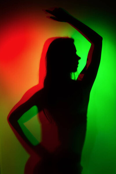 Silhouette of a girl in green and red colour light wearing lingerie shot through matte glass