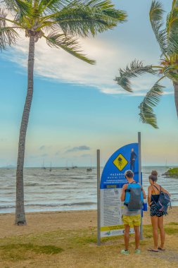 Airlie Beach, Avustralya - 13 Kasım 2016: Tehlikeli Irukandji denizanası hakkında tehlike uyarı işareti okuyan bir erkek ve kadın.