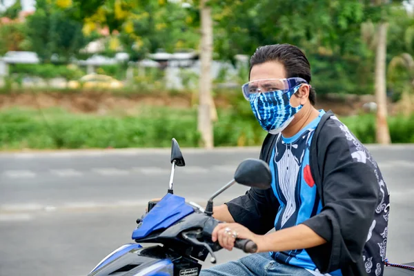 Motosikletli bir adam koruyucu yüz maskesi takıyor..                           