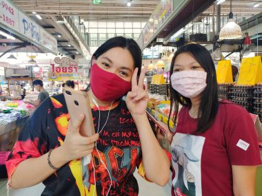 22 Ağustos 2022 'de Pathumthani, Tayland' da çekilmiş, süpermarket pozu veren koruyucu maske takan iki kız..