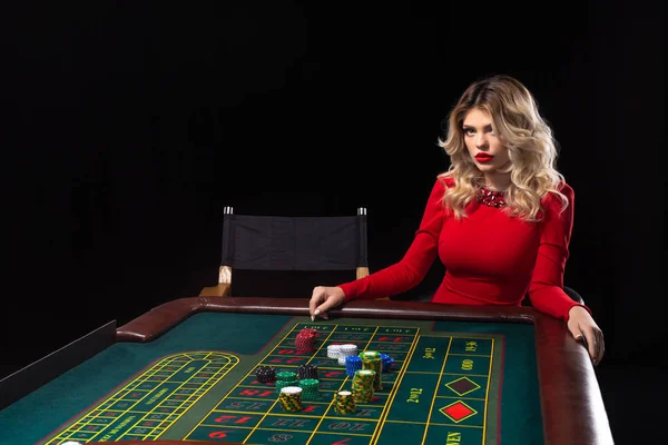 Mladá blond žena nosí krásné červené šaty je hraní rulety v kasinu — Stock fotografie