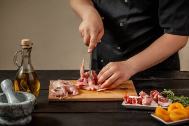 The chef prepares raw quail carcasses in the kitchen. Fresh raw meat quails ready for cooking on the wooden board clipart