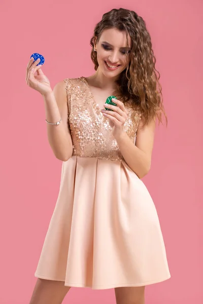 Hermosa mujer joven con fichas de casino sobre fondo rosa — Foto de Stock