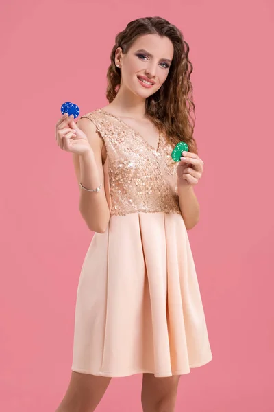 Beautiful young woman with casino chips on pink background