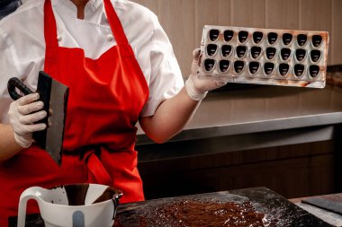 Bir kadın pudra kırmızı üniforma ve beyaz steril eldiven ile sütlü çikolata bir tablo üzerinden bir dizi renkli çikolata yapmak.