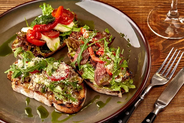 Ιταλικά σάντουιτς - Μπρουσκέτα με πατέ κρέατος, ρόκα, ήλιος αποξηραμένα ντομάτας και τους σπόρους σε ψωμί στο σκοτεινό ξύλινο τραπέζι. — Φωτογραφία Αρχείου