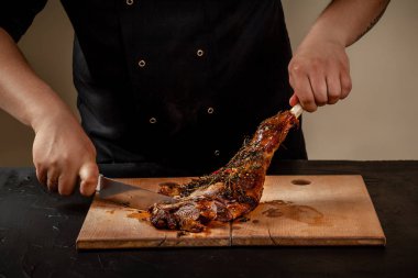Şef kavrulmuş bacak masada ahşap tahta üzerinde kuzu kesiyor