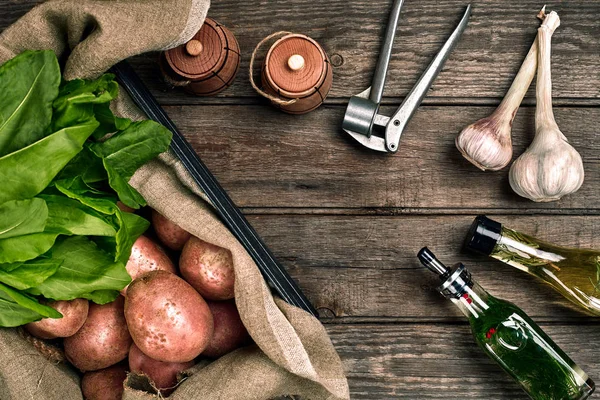 Čerstvé brambory, olej, česnek a kořeněné byliny na pozadí dřevěné kuchyně. — Stock fotografie