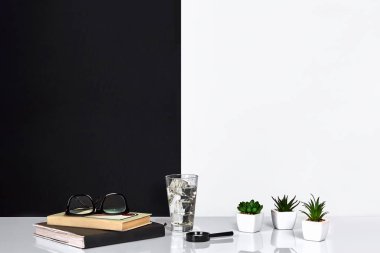 Book, notebook, glasses and a glass of water, black and white wall. clipart