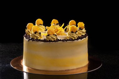 Yuvarlak sarı Doğum günü pastası. Dekoratif kek üzerine krema süslemeleri. Siyah arka plan.