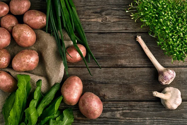 Πρώτων πατάτες σε μια τσάντα λινό, πράσινο κρεμμύδι, χόρτα και σκόρδο, φόντο τροφίμων, κάτοψη — Φωτογραφία Αρχείου